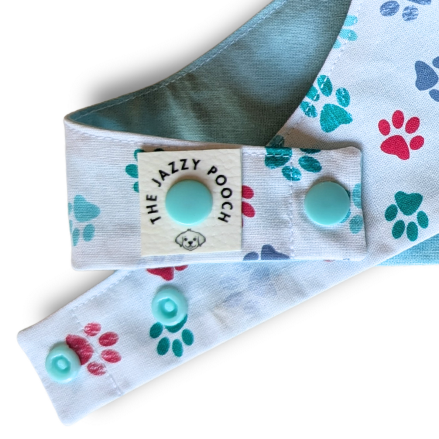 Close-up detail of playful pawprint fabric, adjustable snap-on poppers and The Jazzy Pooch branded label on sustainable dog bandana - The Jazzy Pooch