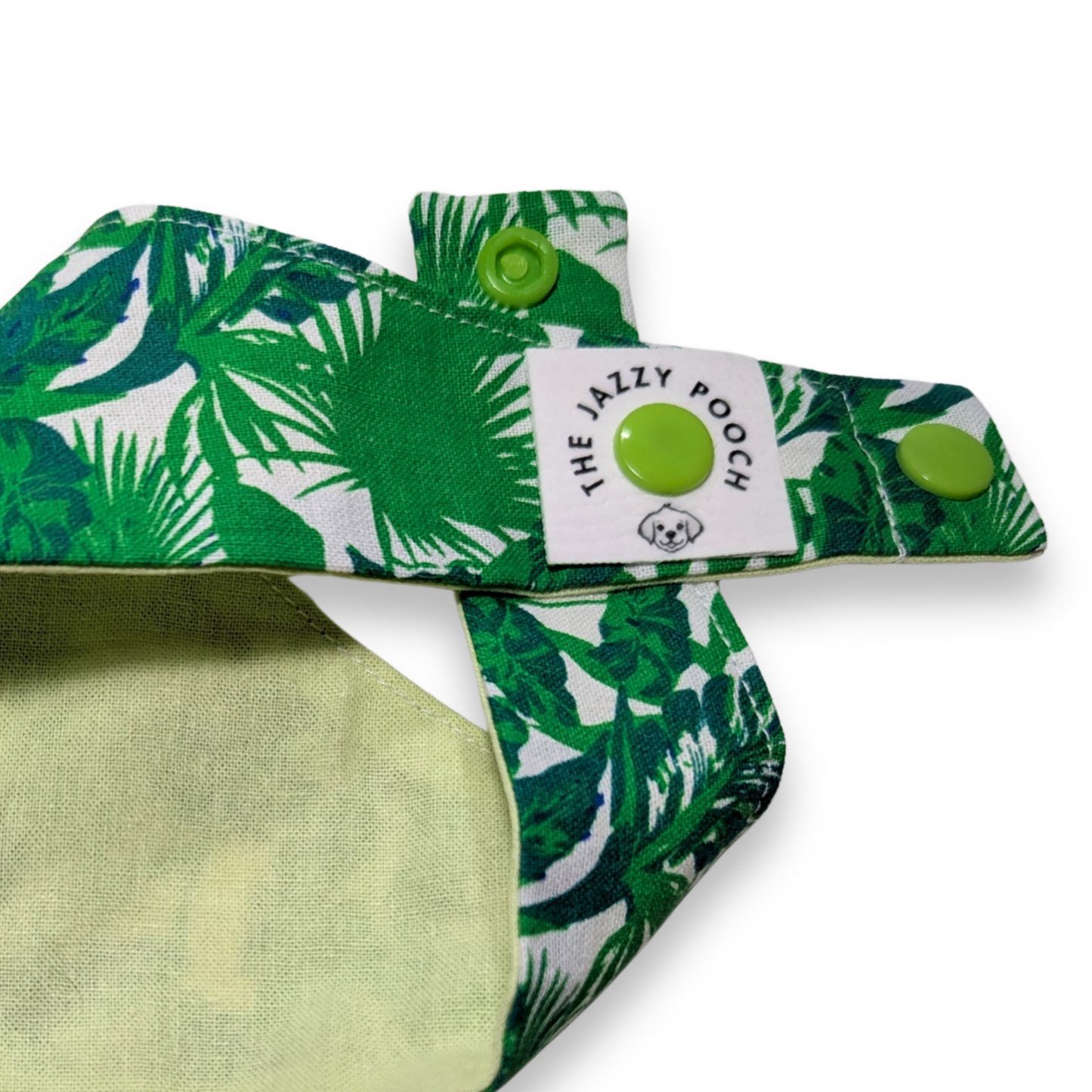 Close-up detail of vibrant jungle foliage fabric, adjustable snap-on poppers and The Jazzy Pooch branded label on sustainable dog bandana - The Jazzy Pooch