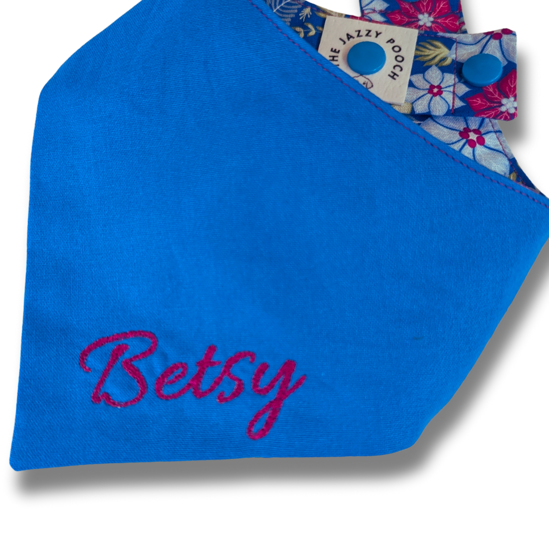 Personalised dog bandana featuring custom embroidered name in dark fuchsia thread on royal blue fabric - The Jazzy Pooch